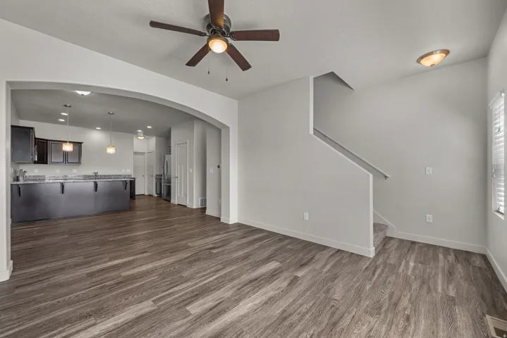 Expansive living area with wood-finish flooring, an arched entryway, and a ceiling fan