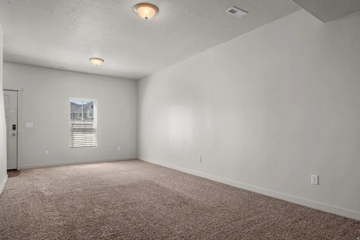 Spacious room featuring neutral carpeting, light-colored walls, and a window with blinds