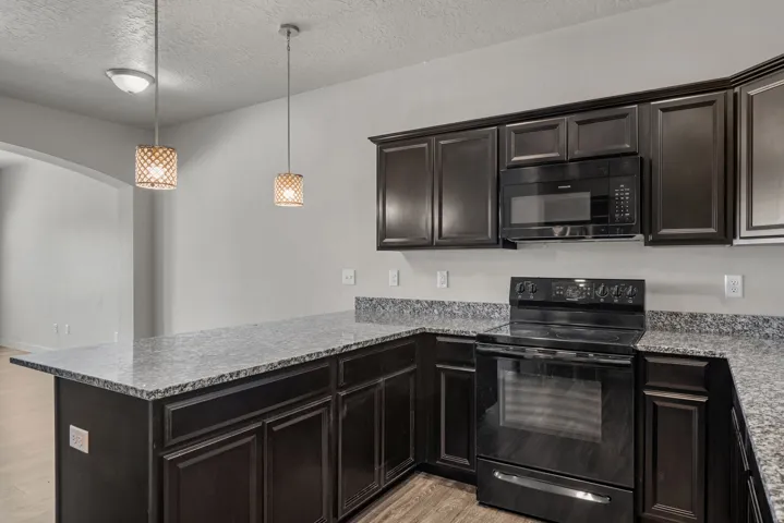 Kitchen featuring dark wood-finish cabinetry, light speckled countertops, and integrated black appliances