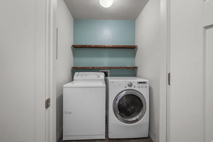 Compact laundry area featuring a front-load washer, top-load washer, and two wood-finish floating shelves