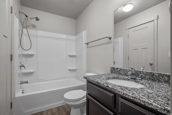 Bathroom featuring a shower/tub combination, vanity with a rectangular basin, granite countertop, and wood-finish flooring