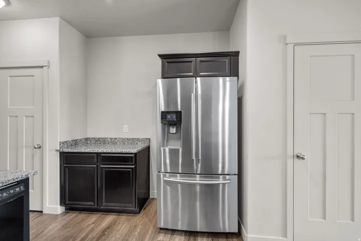 Stainless steel refrigerator, dark wood-finish cabinetry, light-colored countertops, and wood-finish flooring