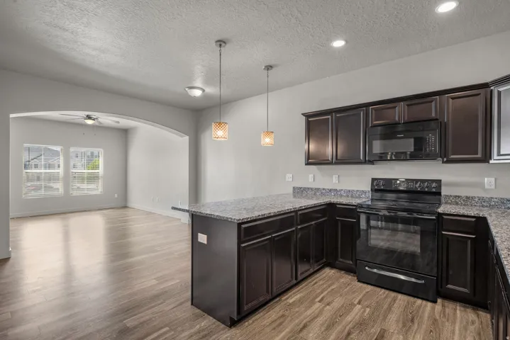 Kitchen featuring dark wood-finish cabinetry, black appliances, and speckled countertops