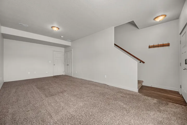 Open area with carpet flooring, a staircase with a wood handrail, and recessed lighting