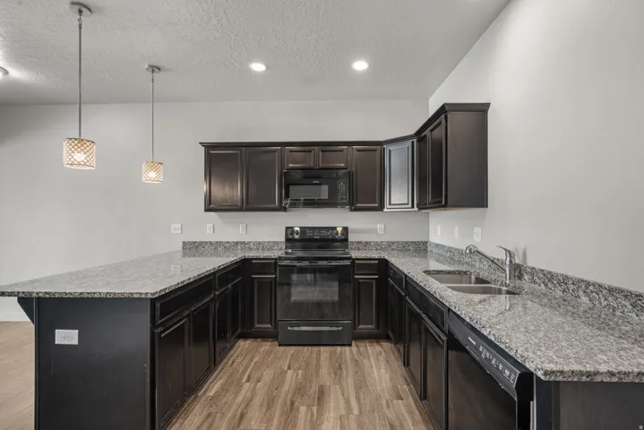 Kitchen featuring dark wood-finish cabinetry, light-toned countertops, a stainless steel double basin sink, and wood-finish flooring