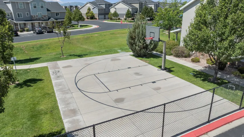 Concrete basketball court with perimeter fencing, surrounded by green lawn and mature trees