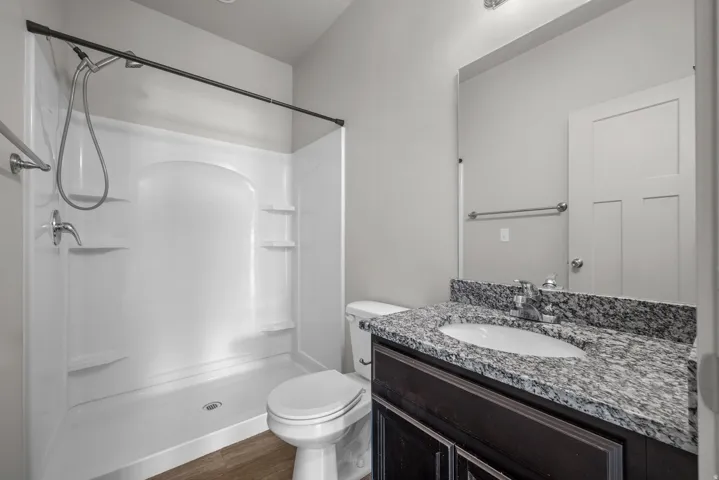 Granite countertop vanity with integrated sink, wood-finish flooring, and a white shower stall with built-in shelving