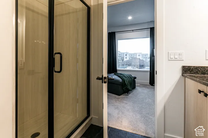 Shower enclosure with black trim and glass door, featuring a light wood-finish tiled interior