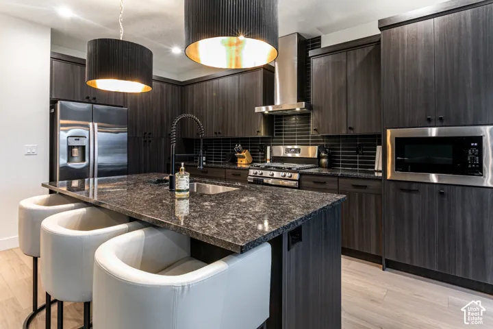 Gourmet kitchen featuring dark wood-finish cabinetry, stainless steel appliances, a large island with a built-in sink, and pendant lighting