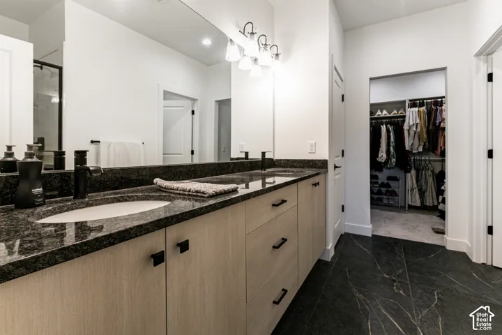 Dual vanity with dark granite countertops and undermount sinks, light wood-finish cabinetry, and black hardware