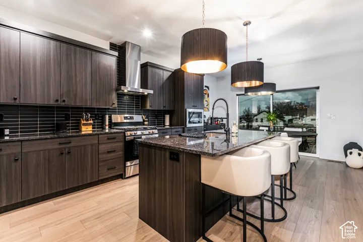 Modern kitchen featuring dark wood-finish cabinetry, built-in stainless steel appliances, a center island with countertop seating, and light wood-finish flooring