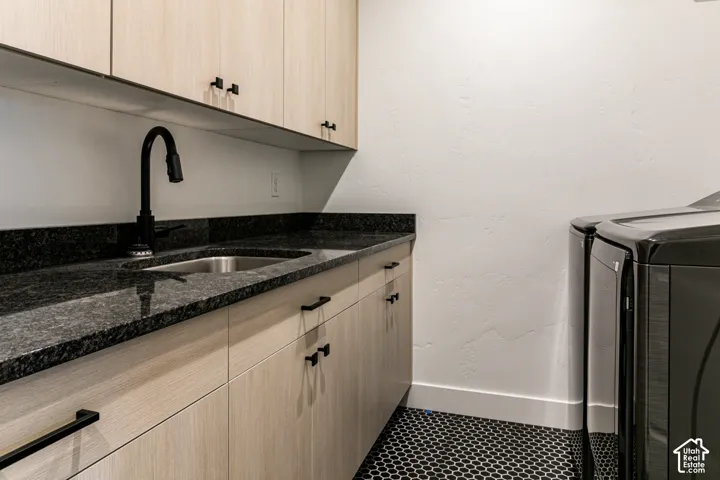 Integrated sink with a matte black faucet, dark stone-finish countertop, light wood-finish cabinetry, and hexagon tile flooring