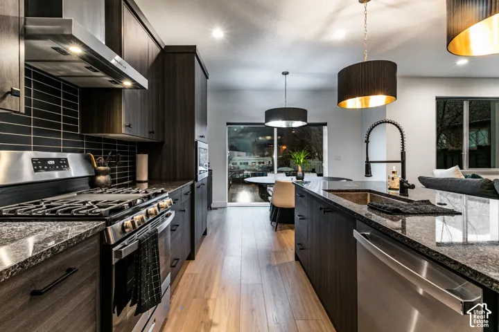 Modern kitchen featuring dark wood-finish cabinetry, stainless steel appliances, dark stone countertops, and a black tile backsplash