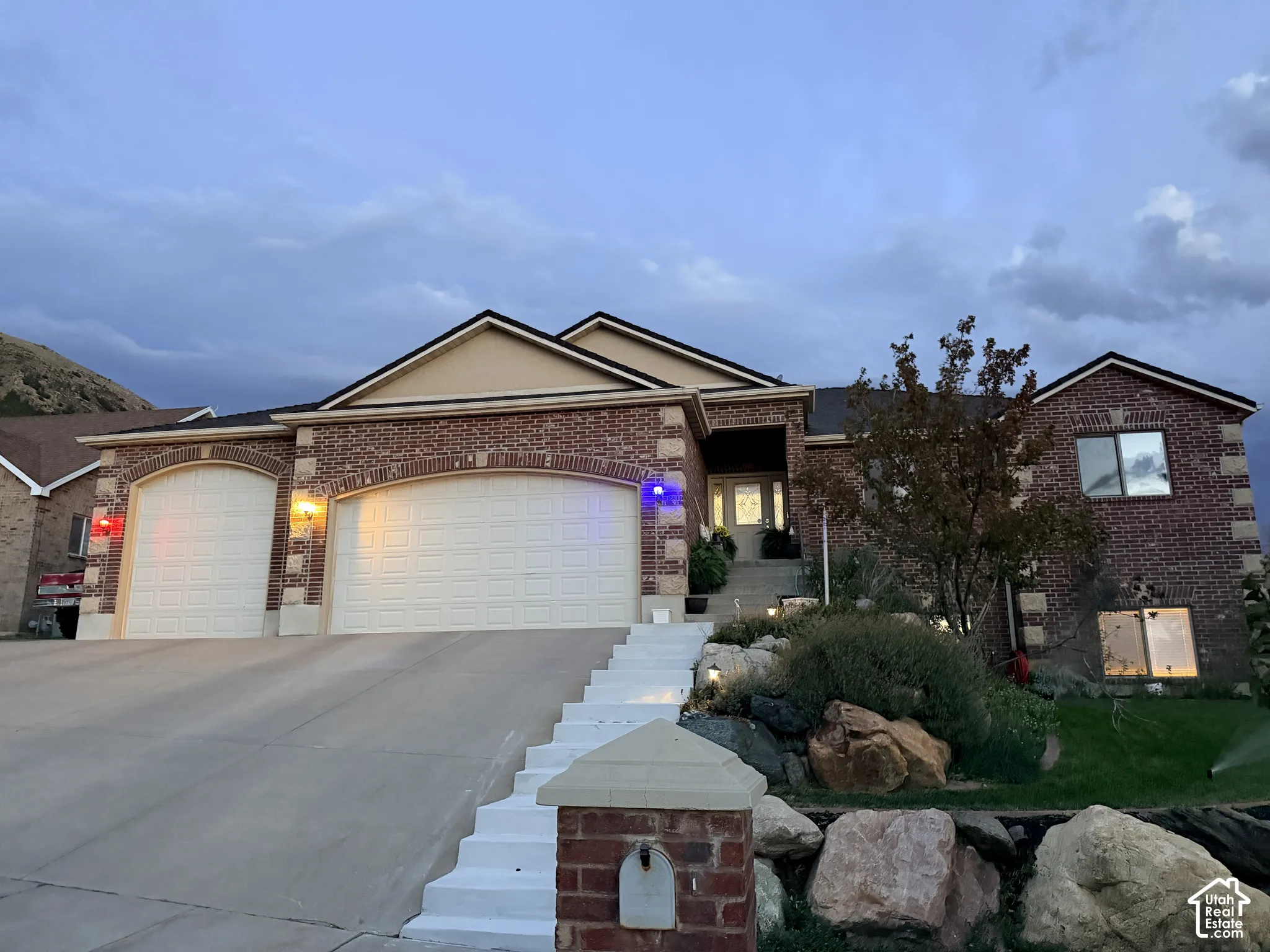 Brick exterior with stone accents, two-car garage, tiered landscaping with rock features, and a front entry with a decorative door