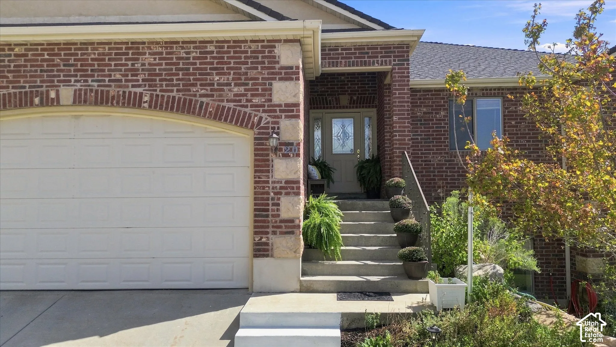 Brick facade with stone accents, a two-car garage, concrete steps leading to the main entry, a covered porch, and a decorative glass front door