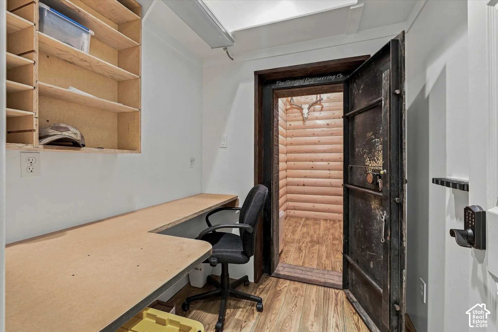 Built-in desk with L-shaped configuration, overhead shelving, wood-finish flooring, and a heavy-duty vault door