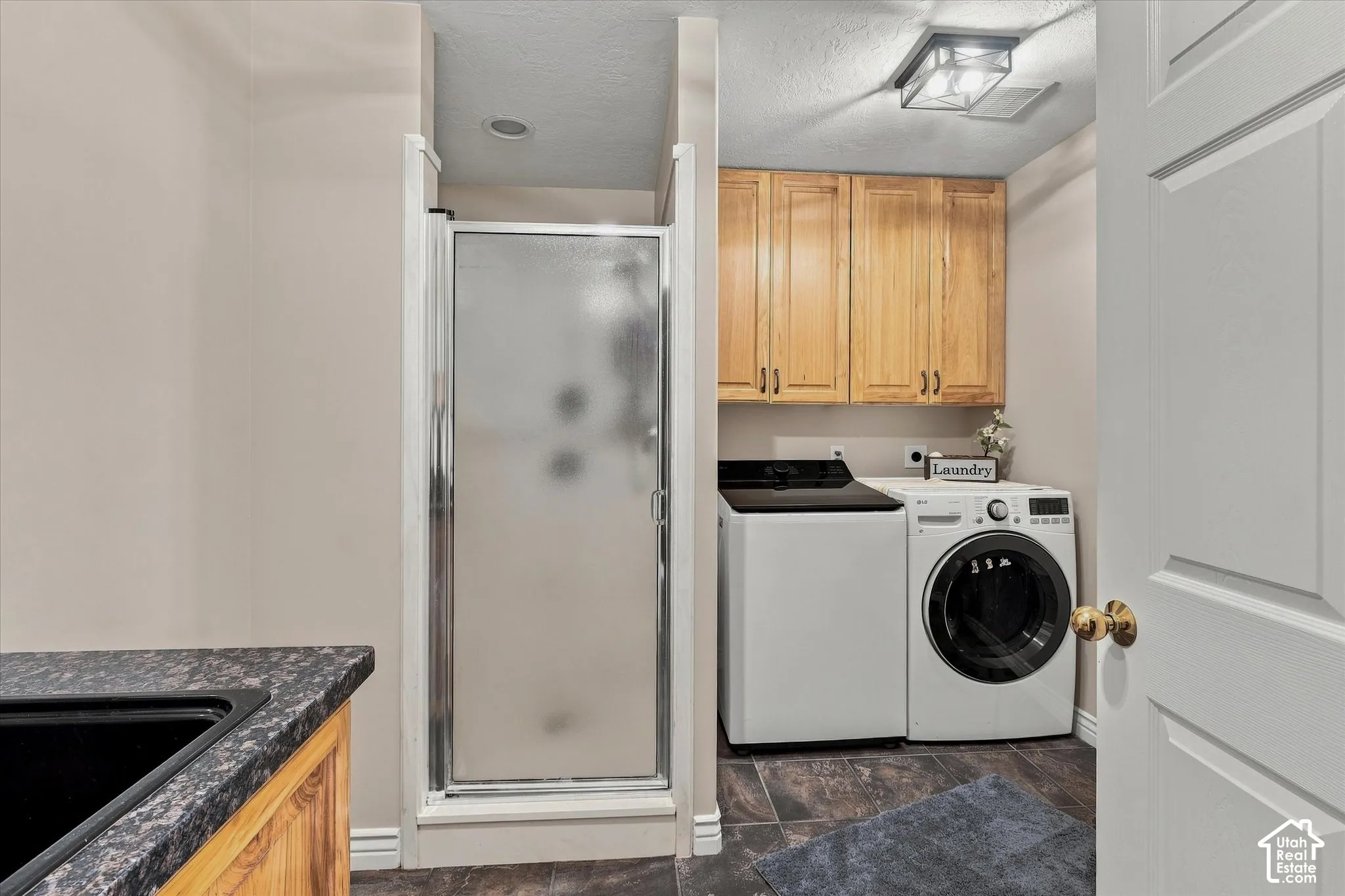 Built-in shower enclosure, wood-finish cabinetry, dark stone-finish countertop, and tiled flooring
