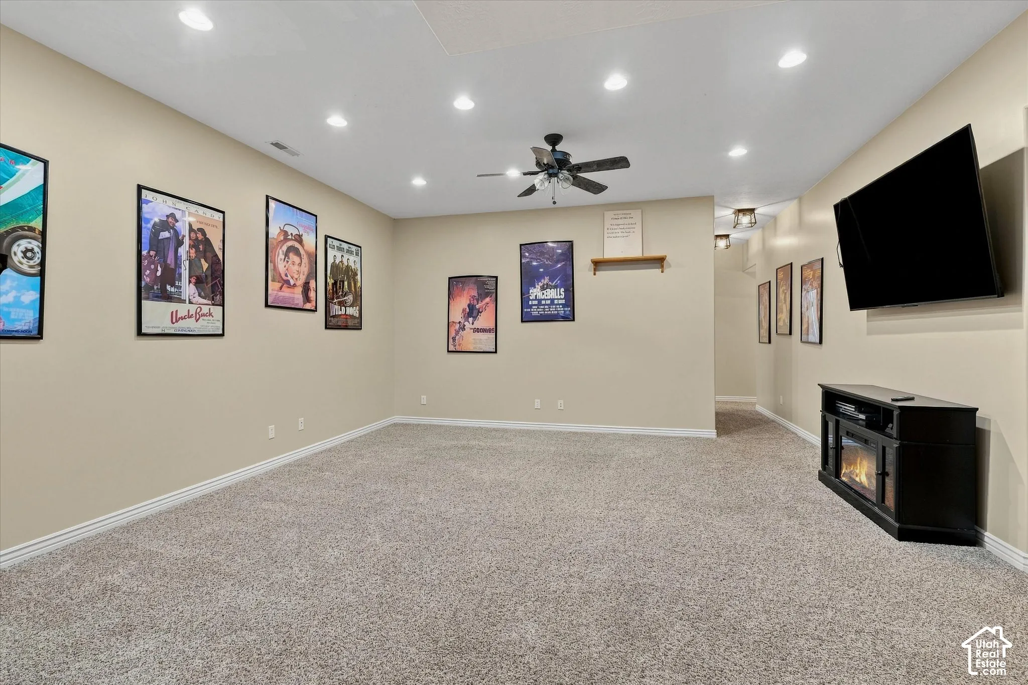 Recessed ceiling lighting, ceiling fan, neutral wall paint, carpet flooring, and a wall-mounted television with an electric fireplace