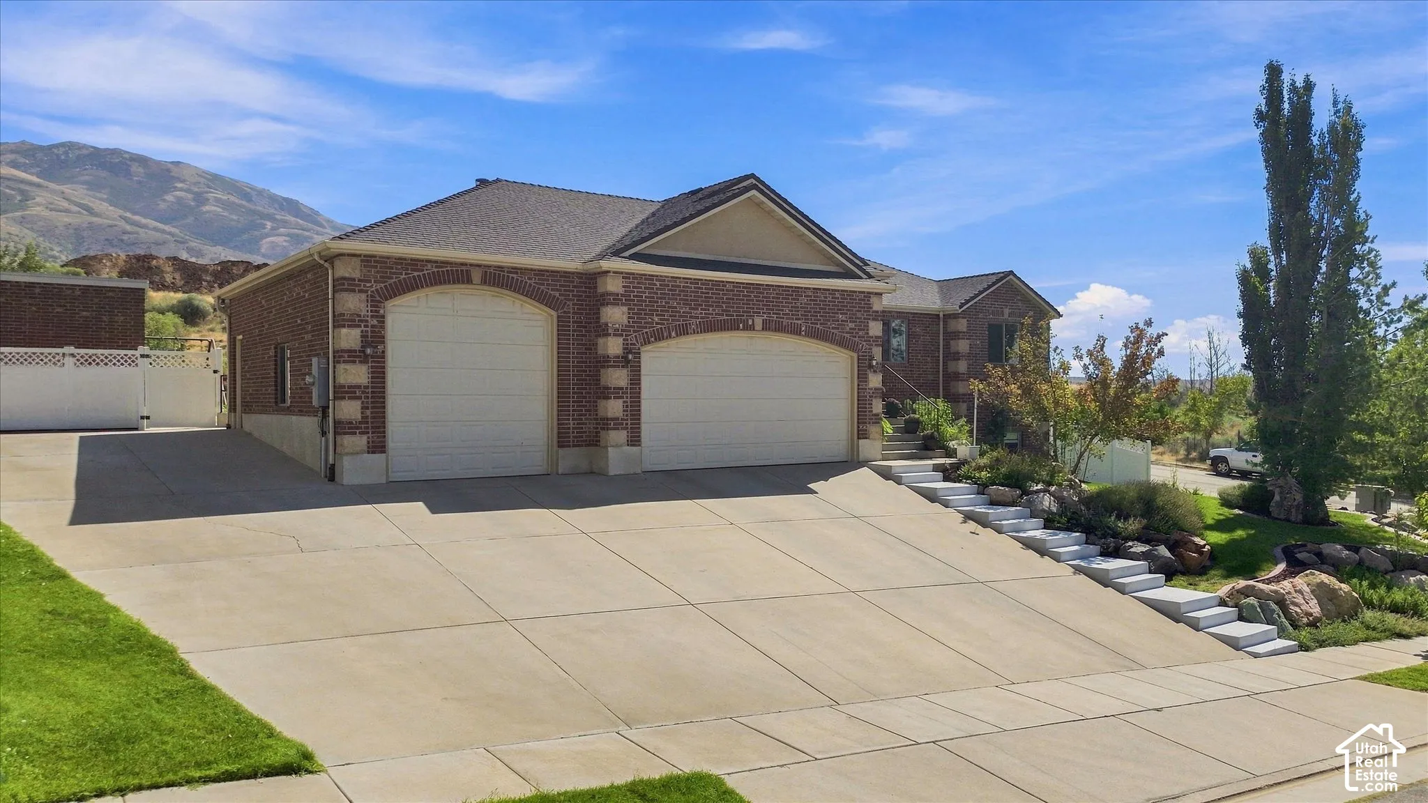 Brick exterior with arched garage door, concrete driveway, stone landscaping, and a mountain backdrop