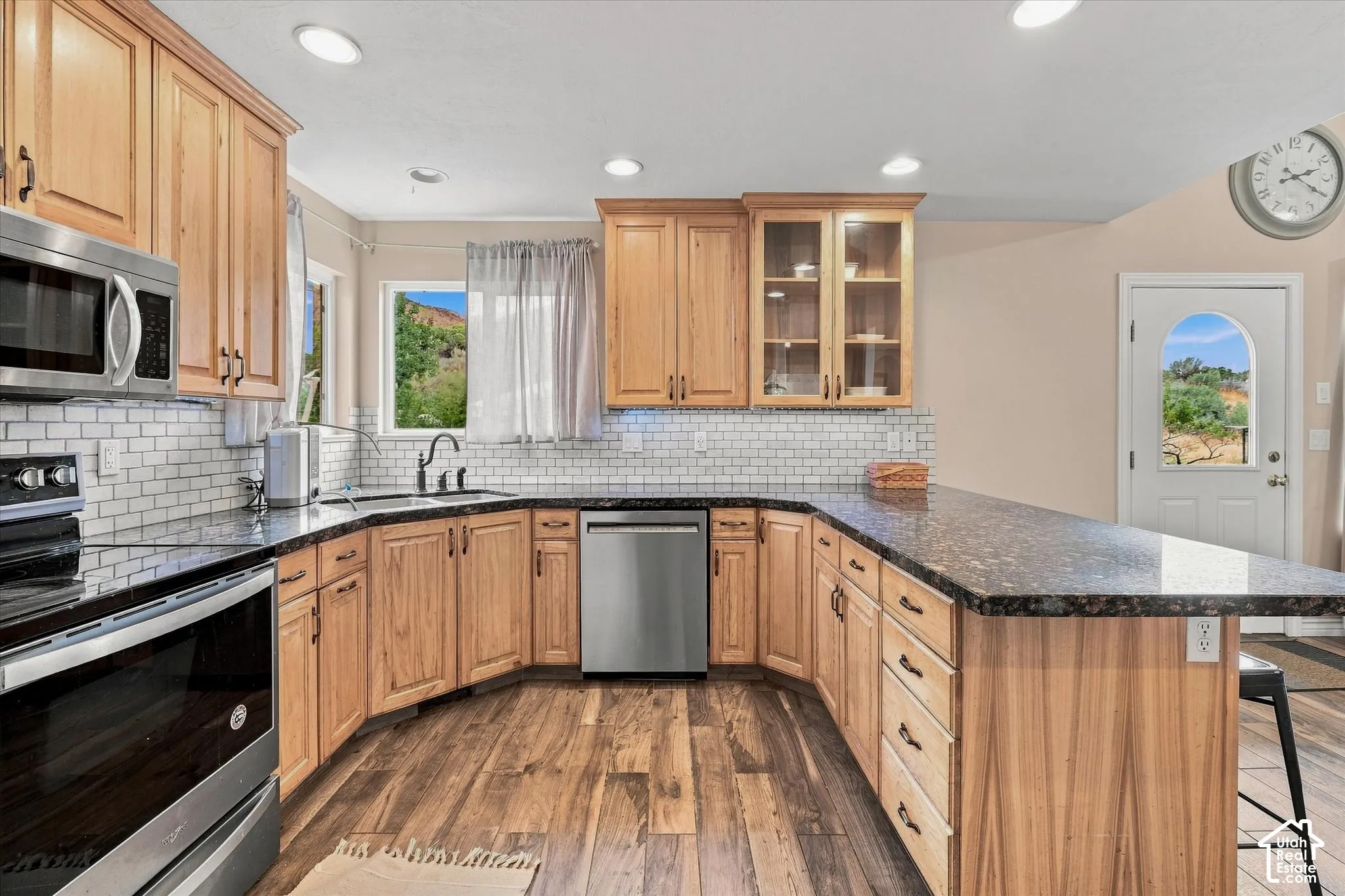Kitchen featuring wood-finish flooring, wood cabinetry, stone countertops, subway tile backsplash, and stainless steel appliances