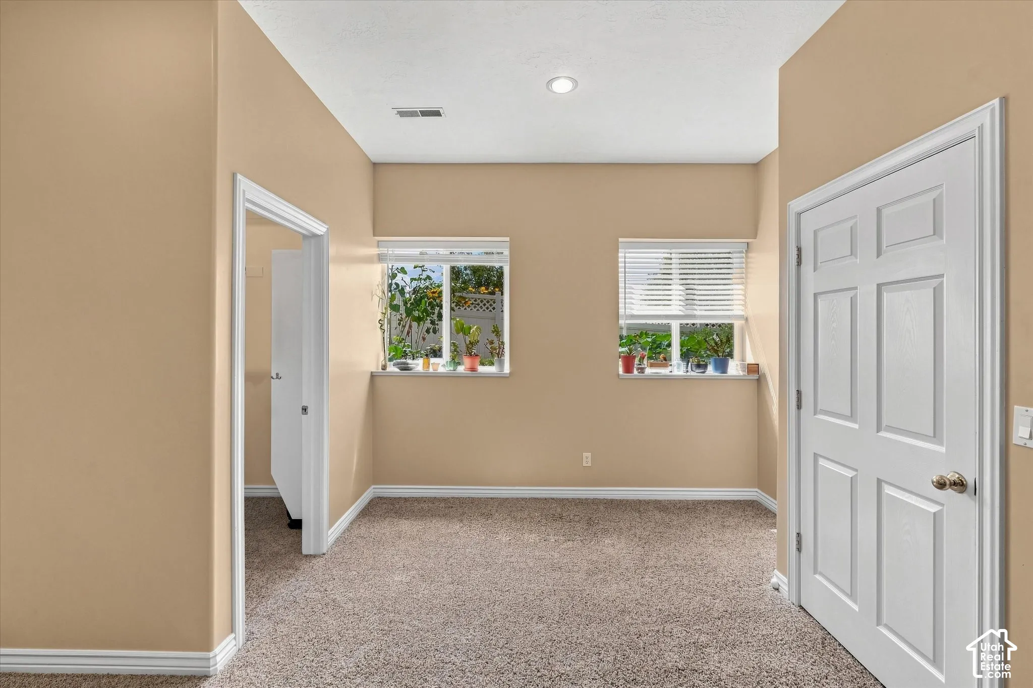 Carpeted flooring with white baseboards, two windows with blinds, recessed ceiling lighting, and a paneled interior door