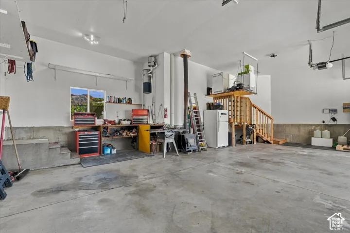 Spacious garage with concrete flooring, integrated workbench, and an elevated storage platform with wood stairs