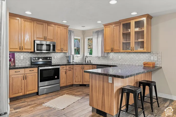 Kitchen featuring wood-finish cabinetry, stainless steel appliances, dark countertops, a subway tile backsplash, and wood-look flooring