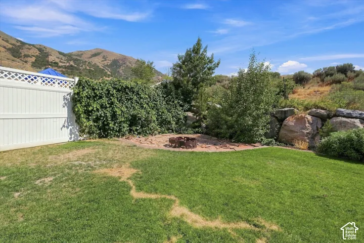 Expansive backyard featuring a brick patio, a decorative fire pit, a white lattice fence, and a rock retaining wall