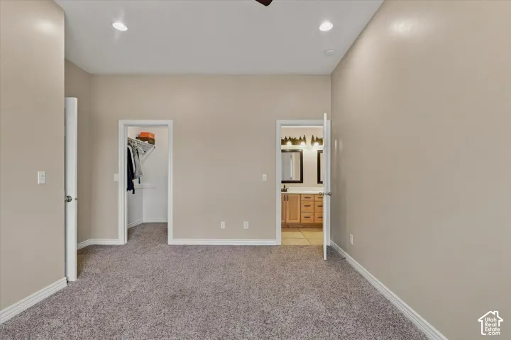Recessed ceiling lighting, textured carpet flooring, walk-in closet, wood-finish vanity with dual sinks, and tile flooring in the bathroom