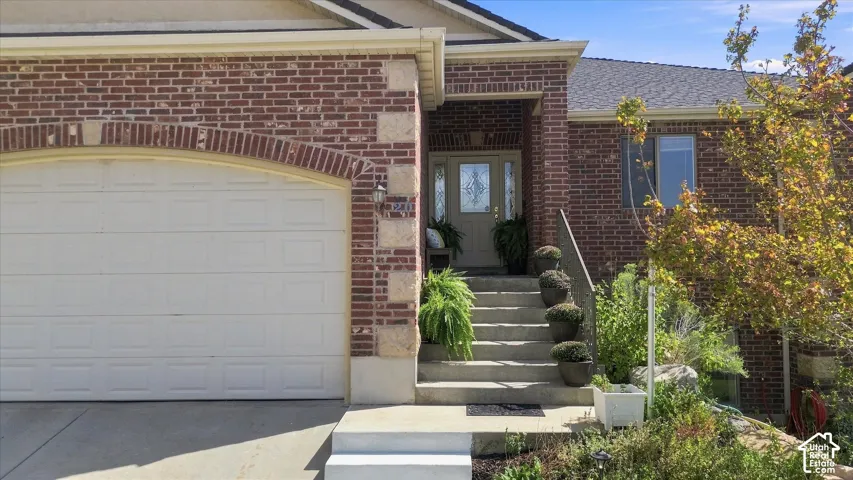 Brick facade with stone accents, a two-car garage, concrete steps leading to the main entry, a covered porch, and a decorative glass front door