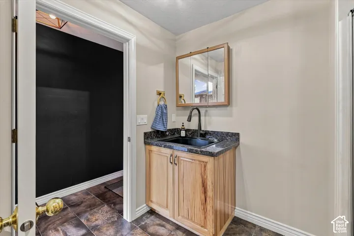 Wood-finish vanity with a dark countertop, black sink, and matte black faucet