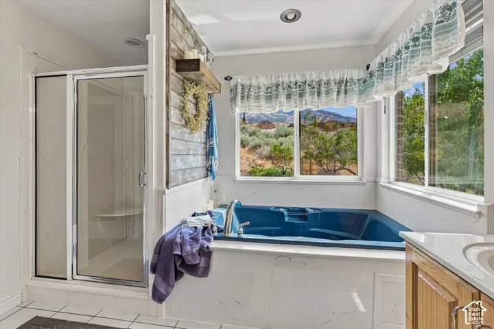 Built-in jetted tub, glass-enclosed shower, wood-finish vanity, recessed lighting, and a prominent window