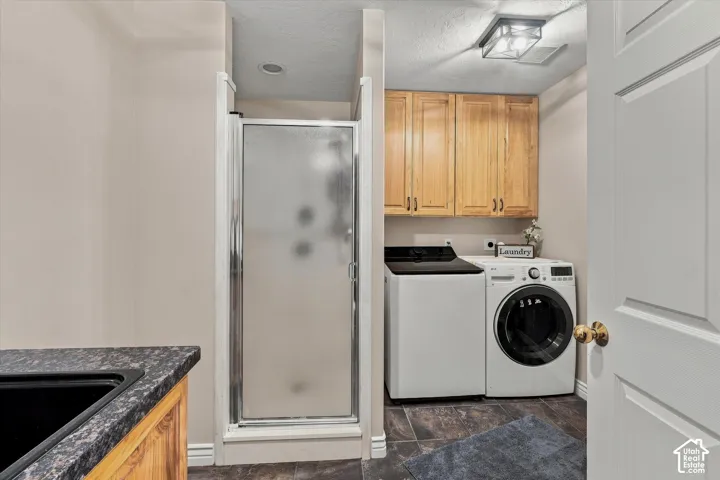 Built-in shower enclosure, wood-finish cabinetry, dark stone-finish countertop, and tiled flooring