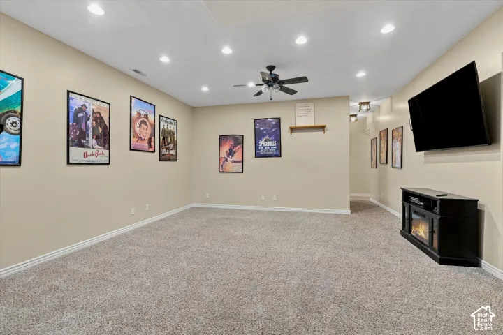 Recessed ceiling lighting, ceiling fan, neutral wall paint, carpet flooring, and a wall-mounted television with an electric fireplace