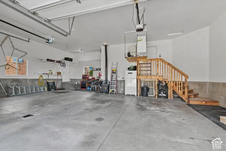 Concrete flooring, built-in shelving, natural wood staircase, overhead garage door opener, and a raised platform
