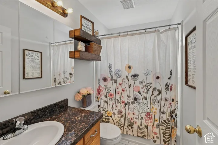 Bathroom featuring a single vanity with an integrated sink, dark speckled countertop, and a wood-finish cabinet