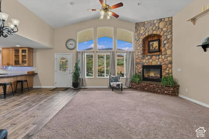 Vaulted ceiling with a ceiling fan, stone fireplace with a brick hearth, multiple arched windows, and wood-finish flooring
