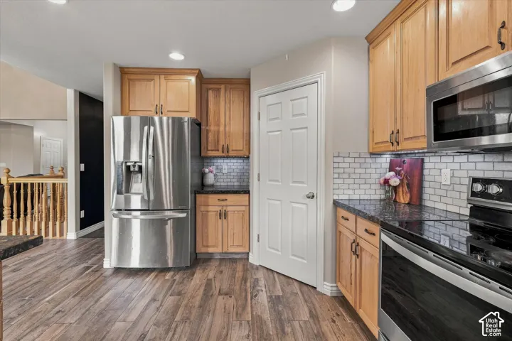 Kitchen featuring wood-finish flooring, stainless steel appliances, light wood cabinetry, and subway tile backsplash