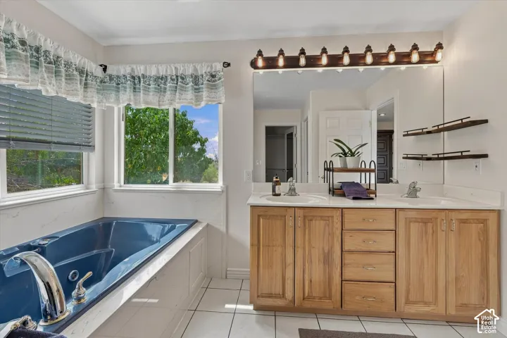 Built-in soaking tub, dual windows, dual vanity with wood cabinetry, and large mirror with integrated lighting