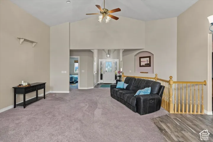 Vaulted ceilings with a ceiling fan, carpet flooring, archway, and wood-finish flooring