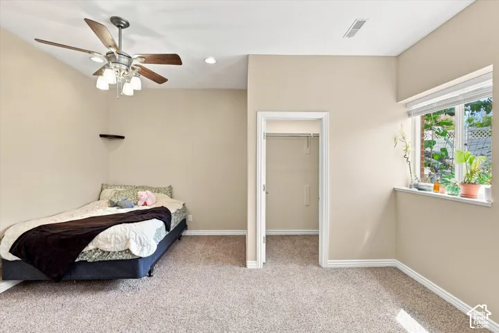 Carpeted room featuring a ceiling fan with integrated lighting, a window with natural light, and a closet with a built-in shelf