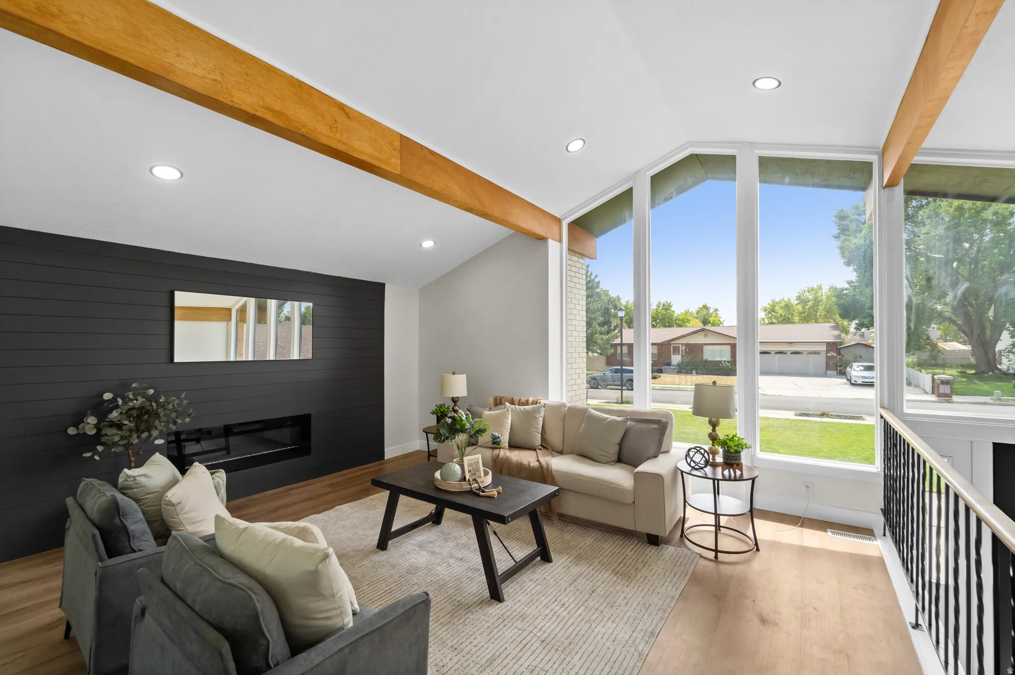 Vaulted ceiling with exposed wood beams, expansive window array, wood-finish flooring, recessed lighting, and a built-in linear fireplace