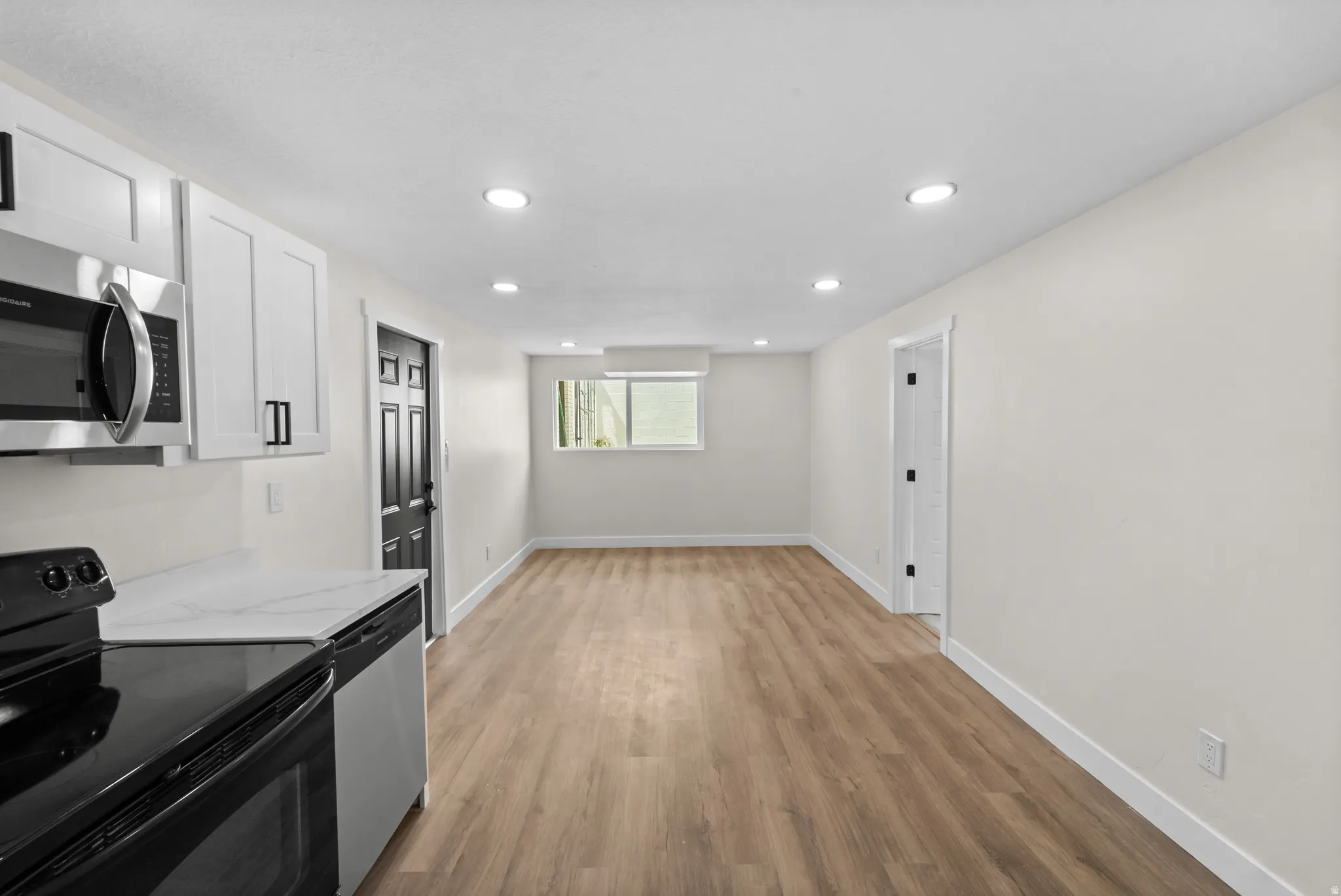Kitchenette featuring white cabinetry, stainless steel microwave, black electric range, and light-toned wood-finish flooring