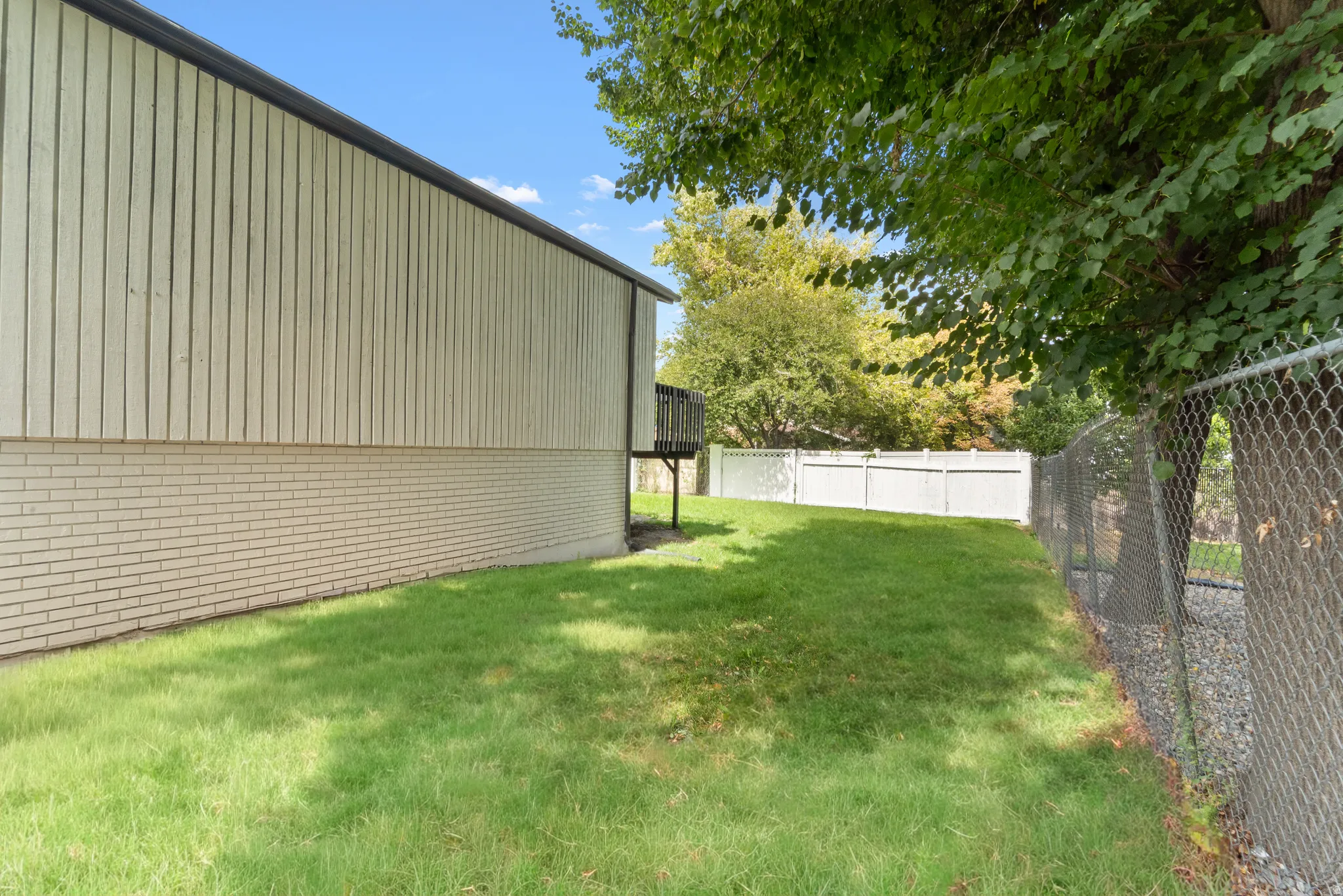 Expansive lawn area bordered by a chain-link fence and a white privacy fence