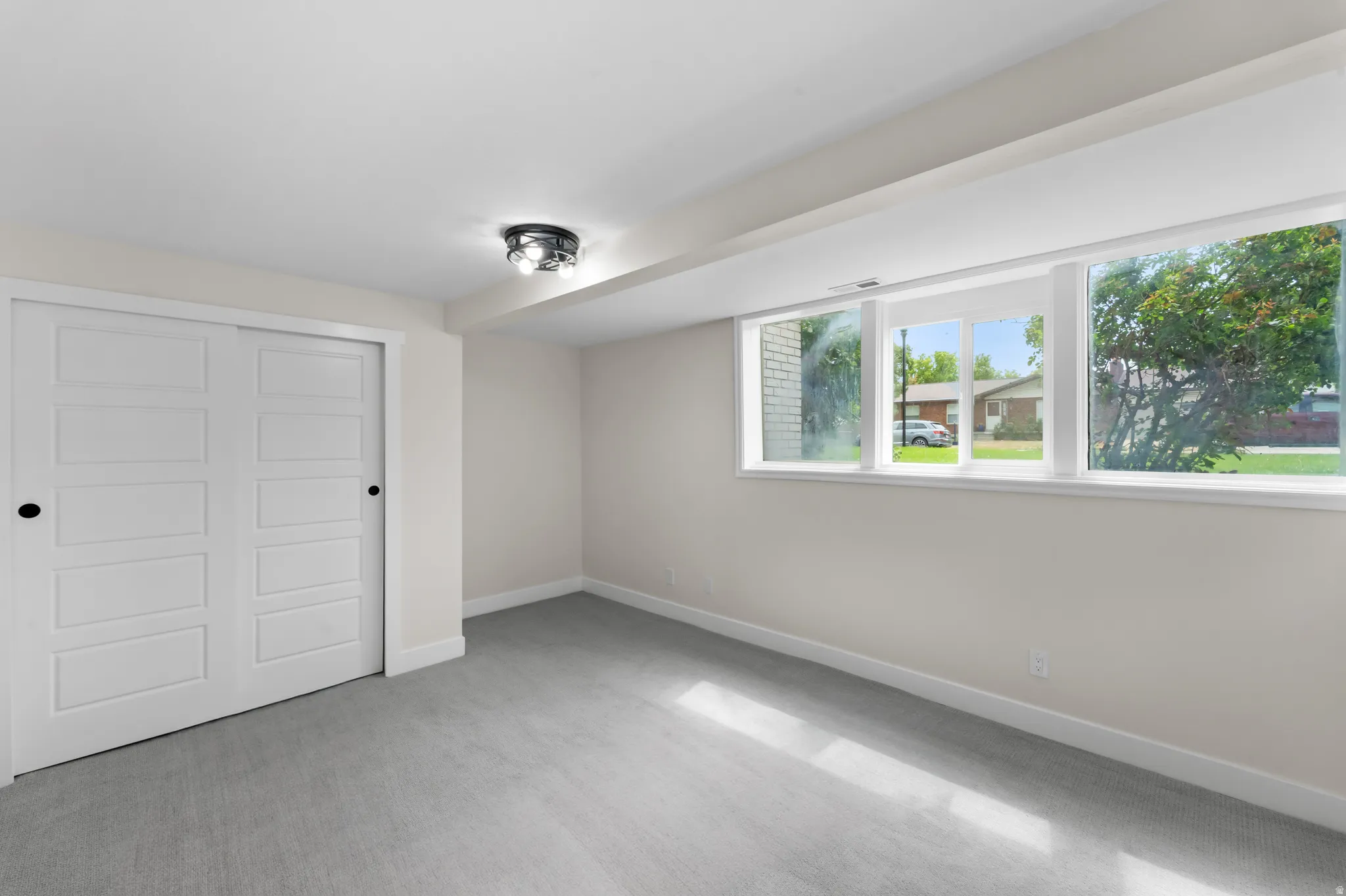 Recessed ceiling light fixture, neutral wall paint, carpeted flooring, sliding closet doors, and a multi-pane window