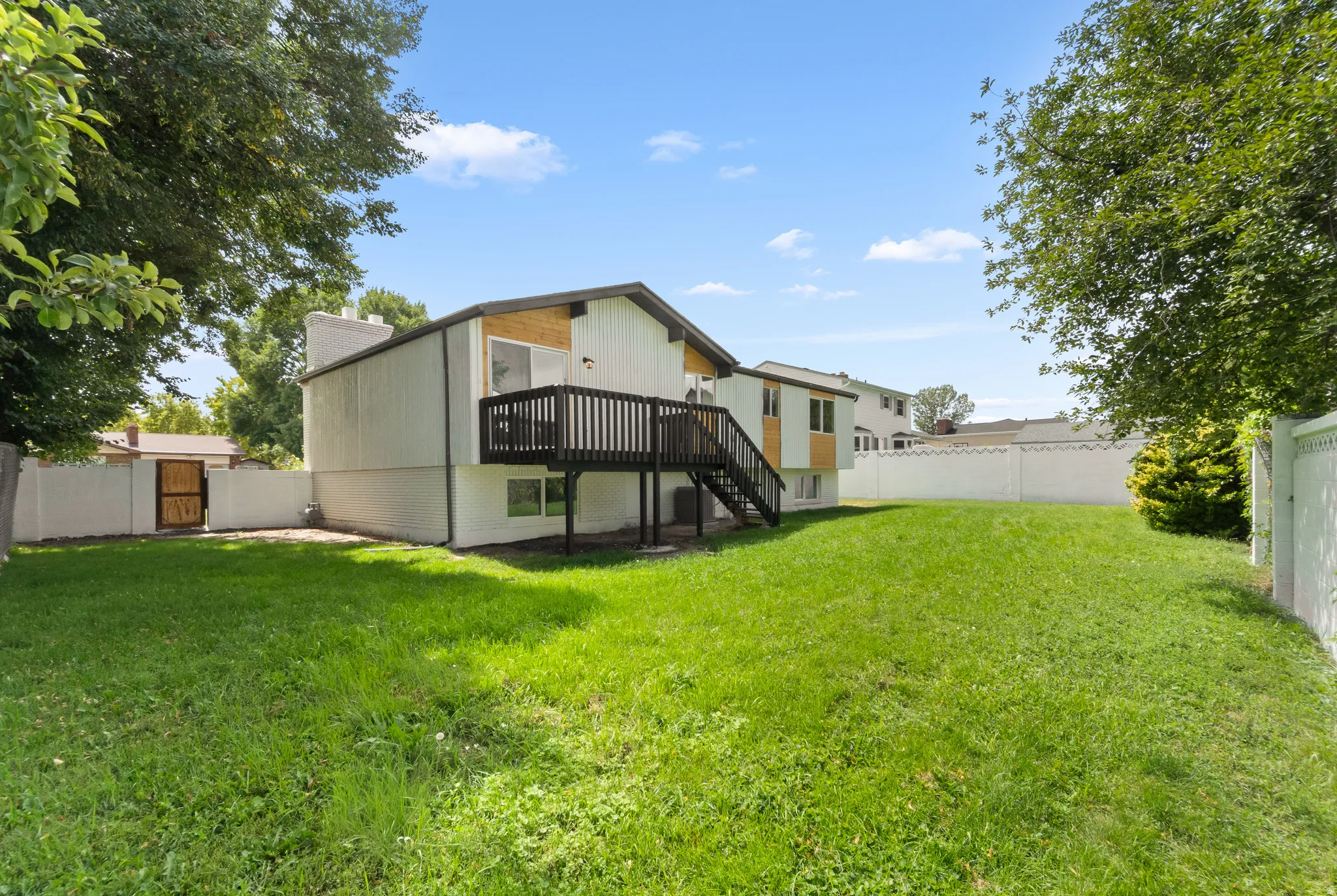Expansive backyard featuring a manicured lawn, a privacy fence, and an elevated wood deck with stairs