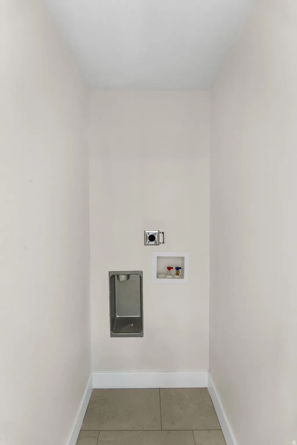 Recessed dryer vent hookup, washing machine hookups, and a utility basin, all set against neutral walls and tiled flooring
