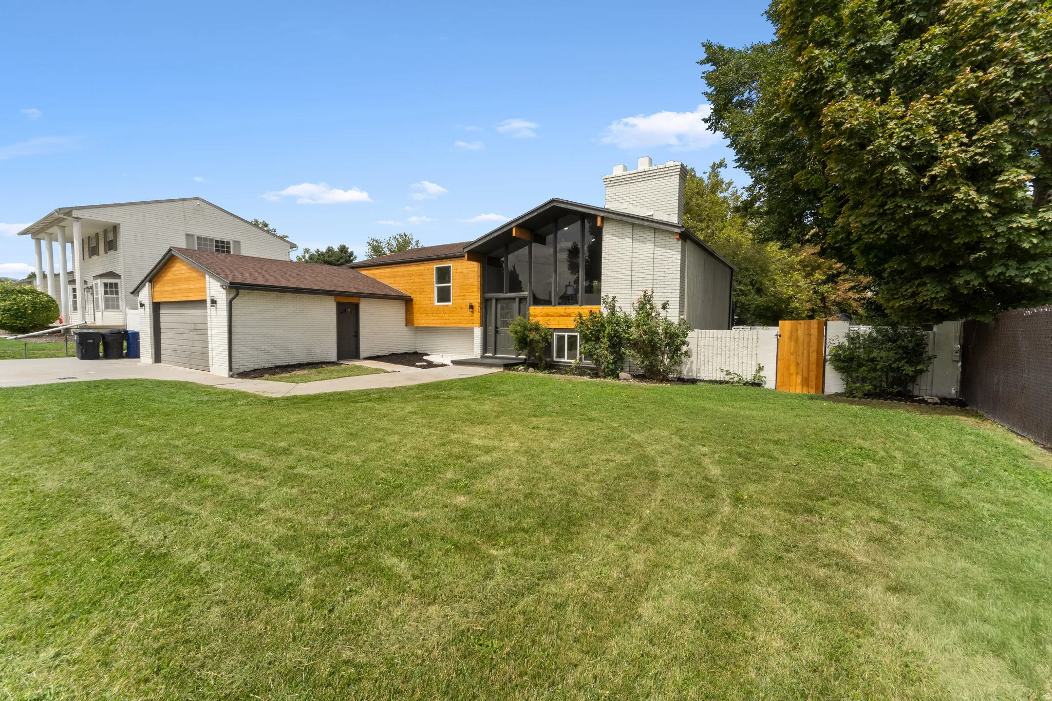 Modern architectural home featuring a large front lawn, attached garage, wood-paneled accents, and extensive windows