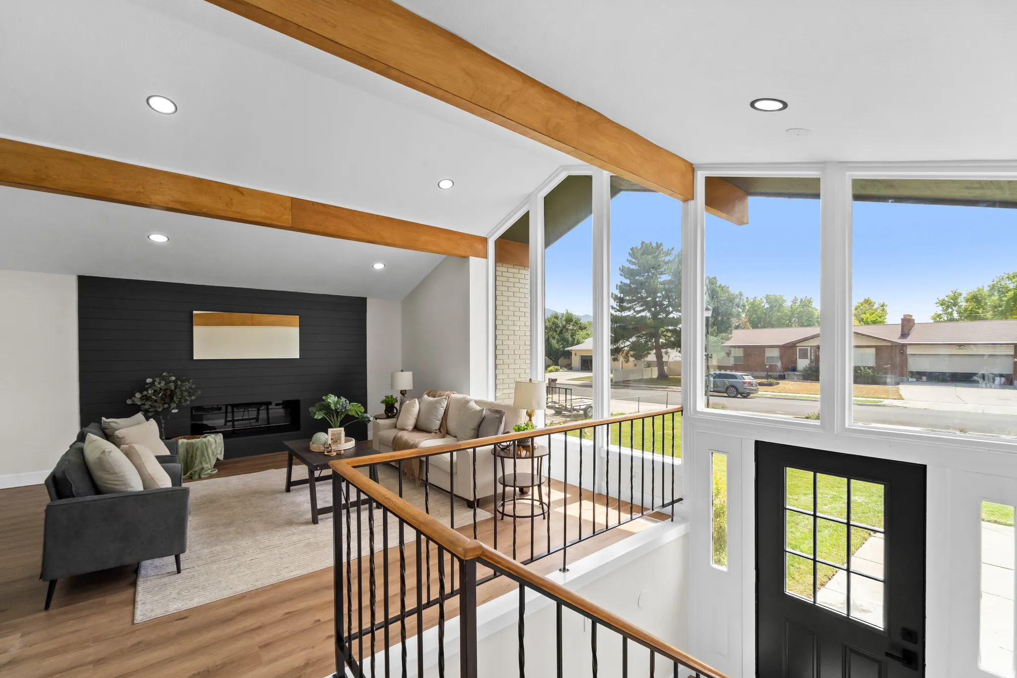 Vaulted ceiling with exposed wood beams, expansive window wall, contemporary fireplace with shiplap accent wall, recessed lighting, and wood-finish flooring