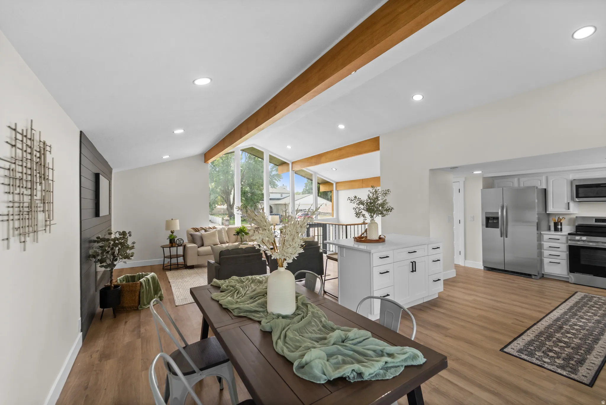 Vaulted ceilings with exposed wood beams, recessed lighting, wood-finish flooring, and a kitchen featuring stainless steel appliances
